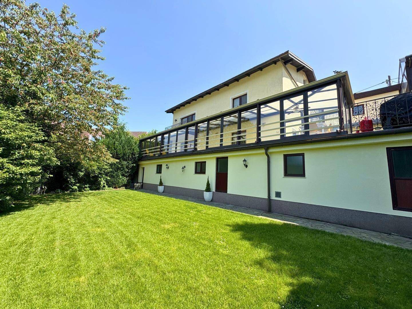 Gepflegter Rasenbereich hinter dem Haus mit einem Wintergarten und viel Grün.