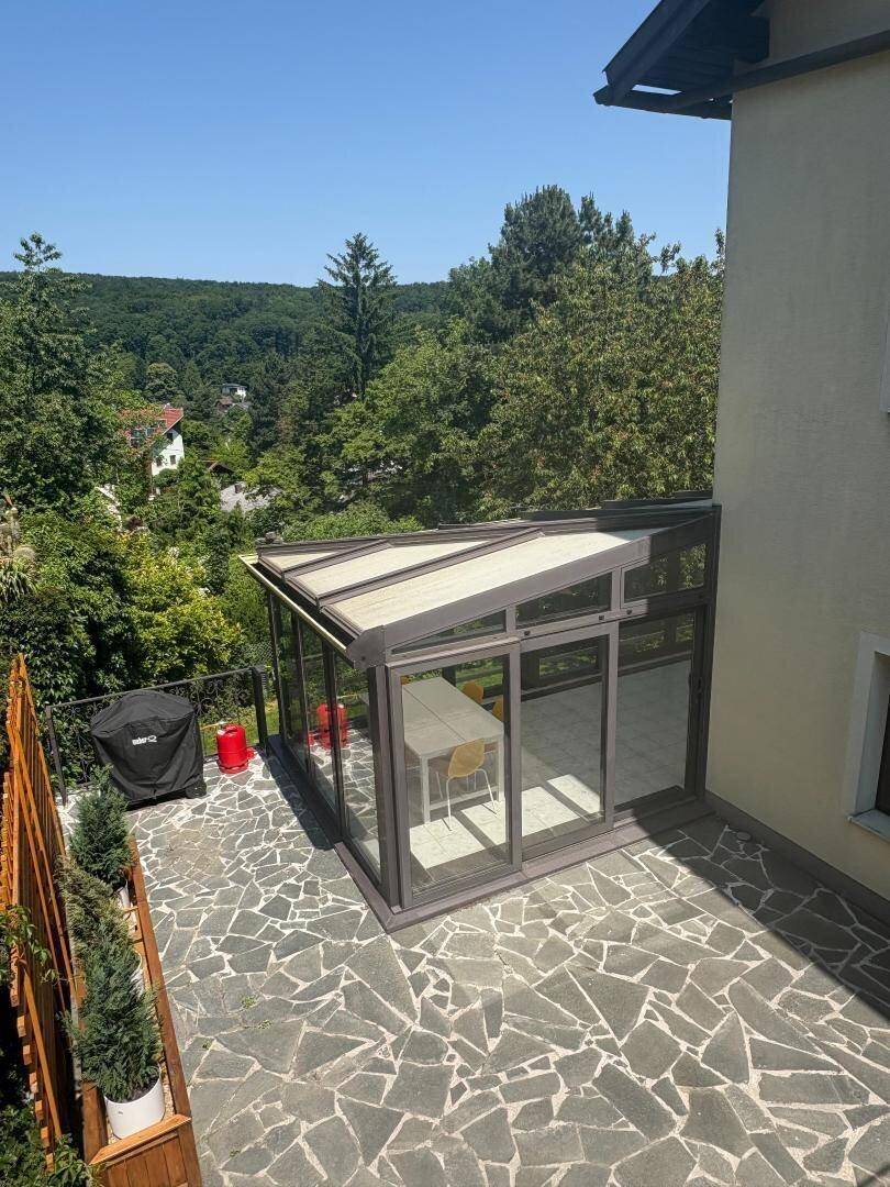 Große Steinterrasse mit kleiner Glaskonstruktion und weitem Blick über die Baumwipfel.
