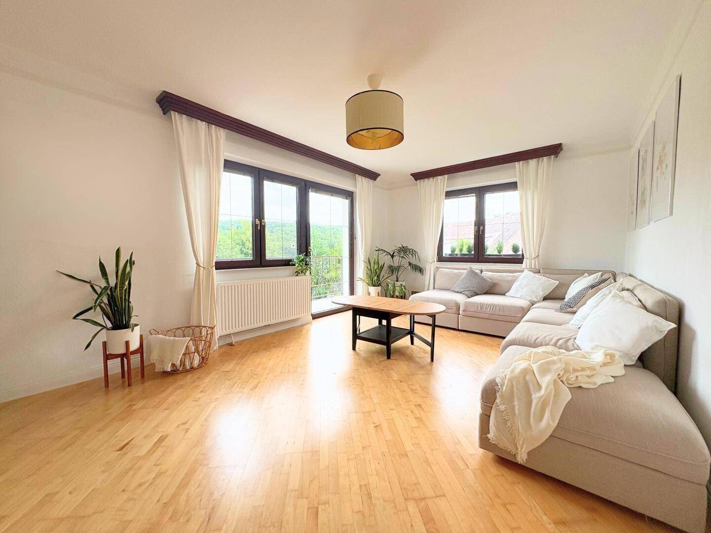 Helles Wohnzimmer mit Holzparkett, großem Sofa und Zugang zu einem Balkon.