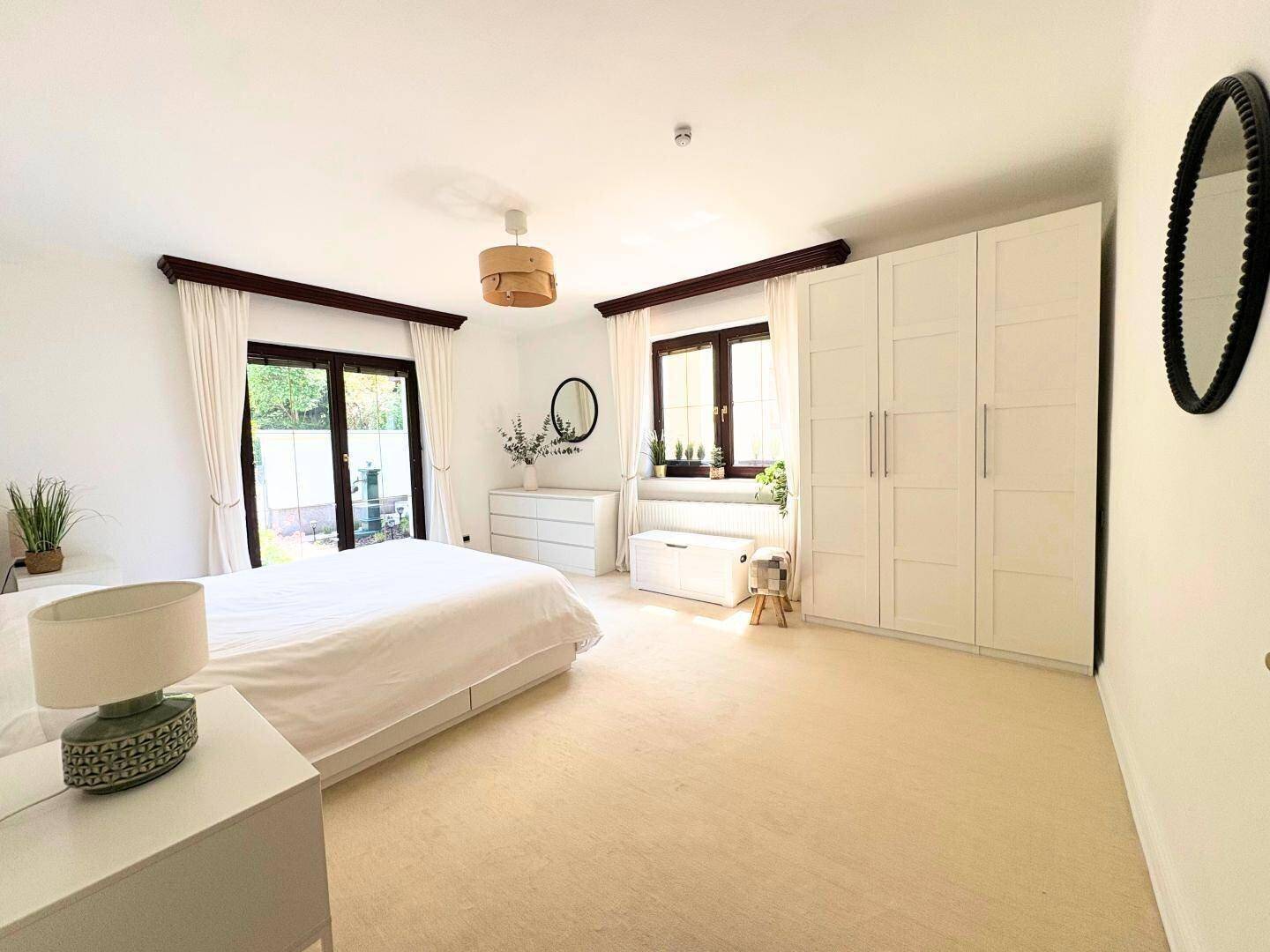 Geräumiges Schlafzimmer mit Teppichboden, weißen Einbauschränken und Zugang zum Garten.