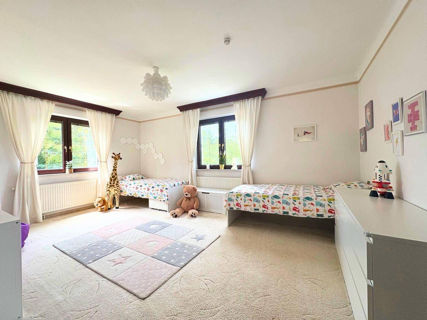 Helles Kinderzimmer mit zwei Betten, Teppichboden und Blick ins Grüne.