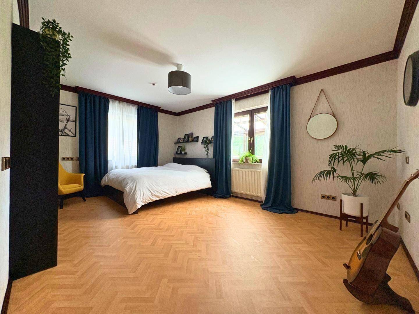 Modern eingerichtetes Schlafzimmer mit Fischgrätparkett und blauen Vorhängen.