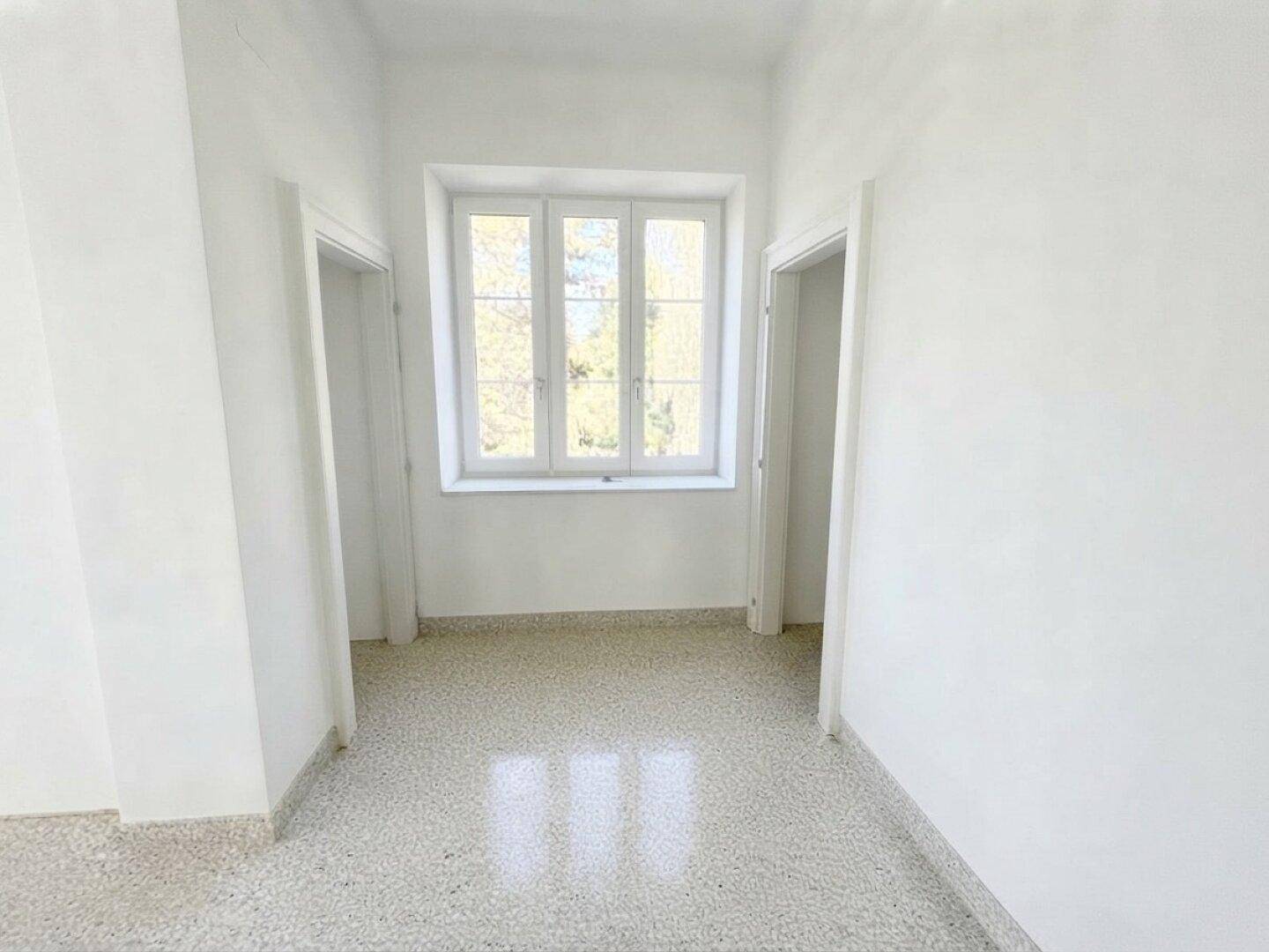 Heller Flur mit Terrazzoboden und weißen Wänden, der zu weiteren Räumen führt.
