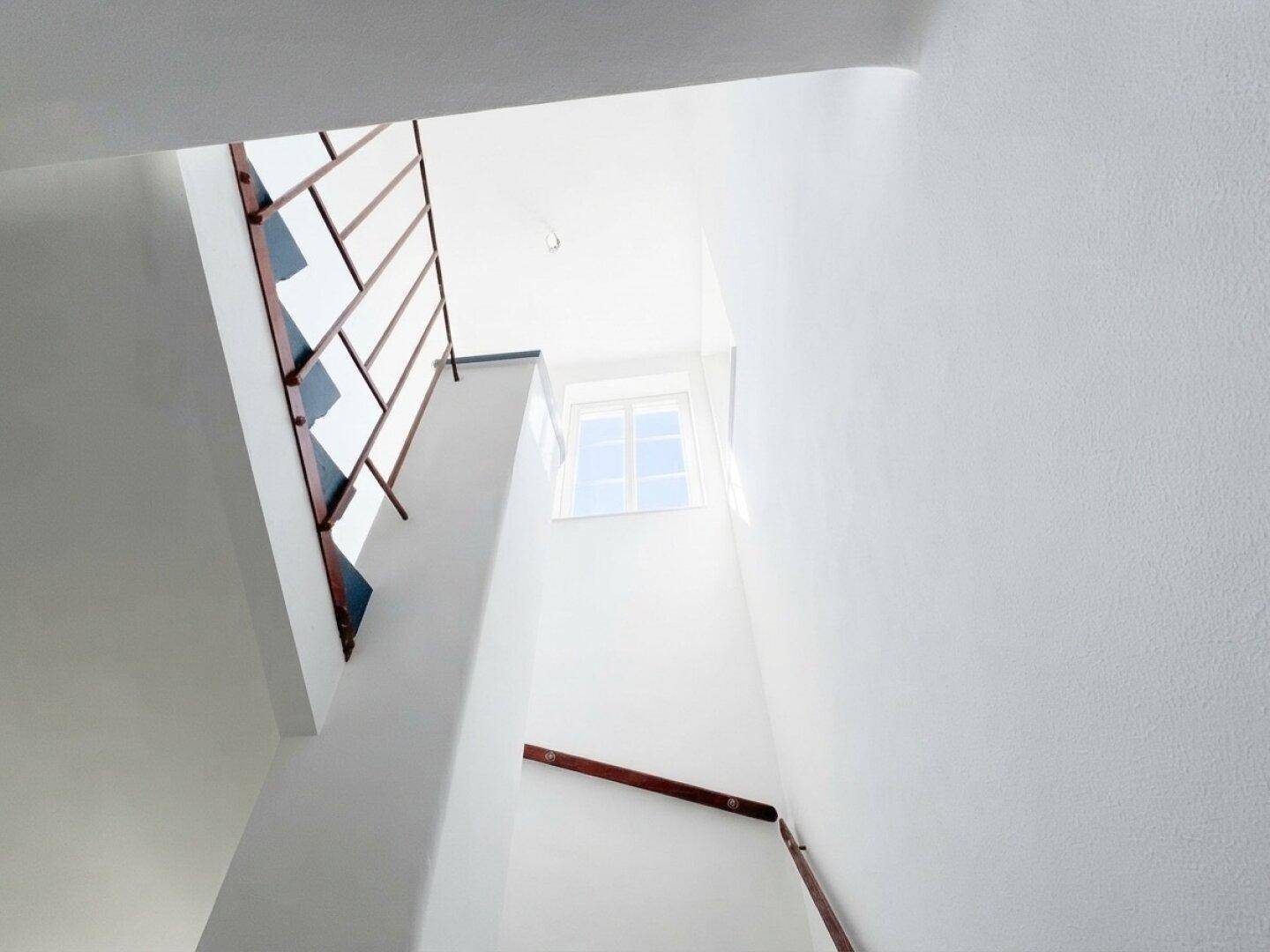 Heller Treppenaufgang mit weiß gestrichenen Wänden und einem Fenster für natürliches Licht.