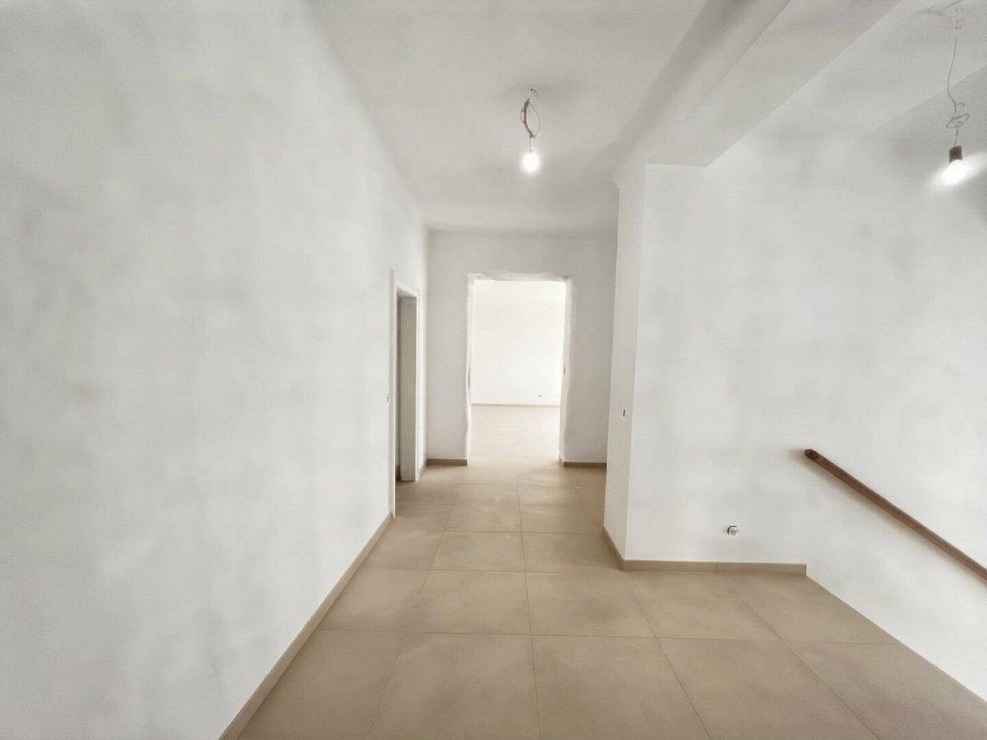 Langer Flur mit hellen Fliesen und weißen Wänden, der zu verschiedenen Räumen führt.
