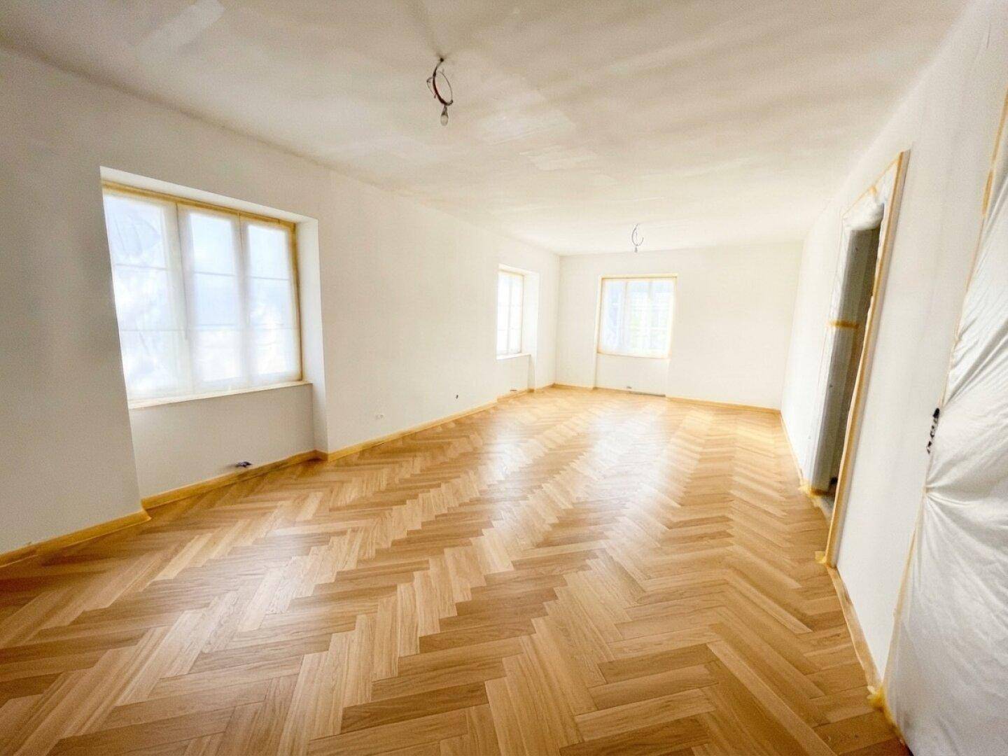 Großes Zimmer mit neuem Fischgrätparkett und hellen Wänden, ideal als Wohn- oder Schlafzimmer.