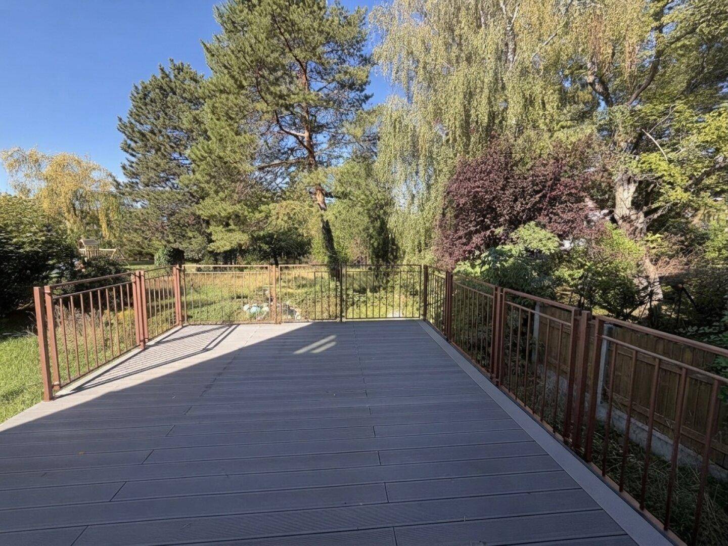 Geräumige Holzterrasse mit Metallgeländer und weitem Blick in den grünen Garten.