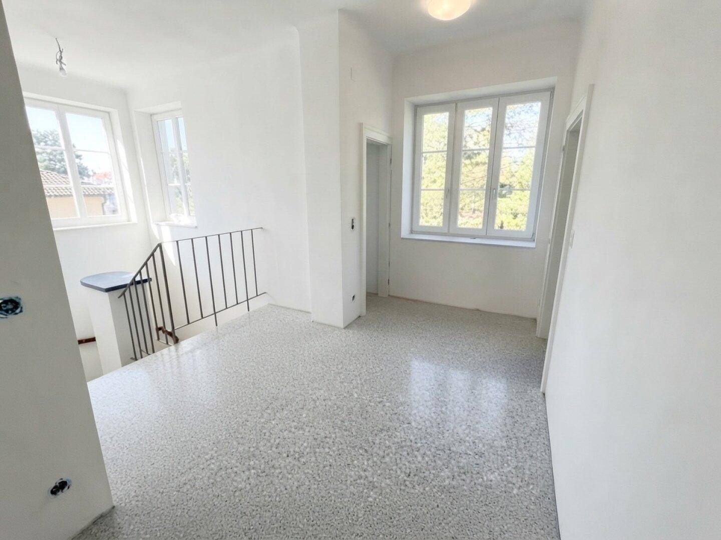 Heller Treppenabsatz mit Terrazzoboden und Fenstern, die den Raum mit Licht füllen.