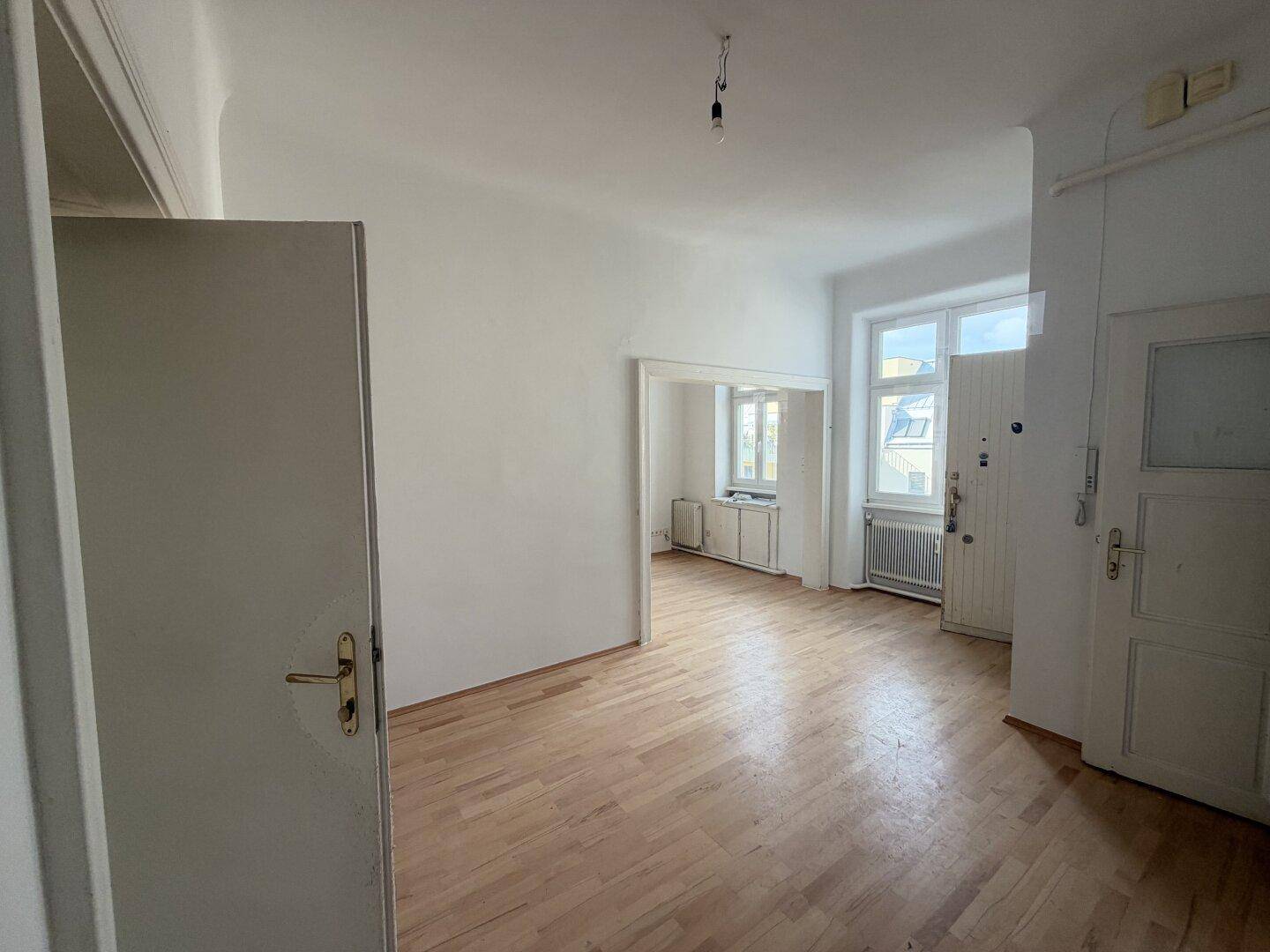 Heller Wohnbereich mit Parkettboden und Zugang zu weiteren Räumen, ideal für offenes Wohnen.