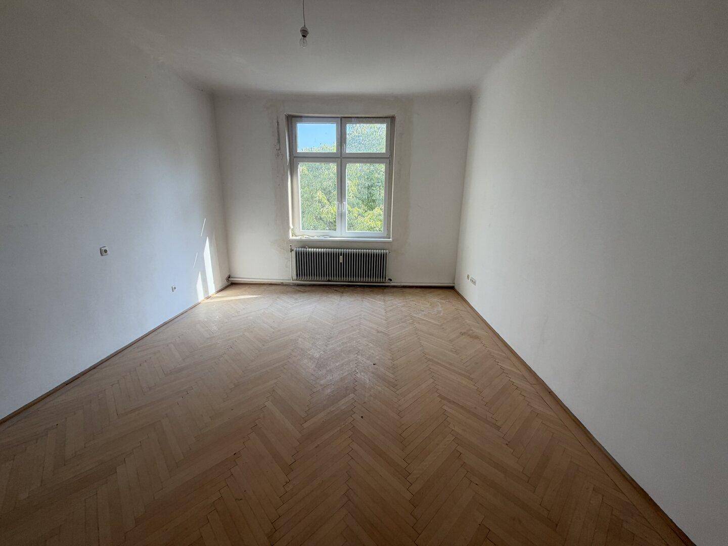 Ruhiges Zimmer mit Fischgrätparkett und einem großen Fenster, das viel Tageslicht spendet.