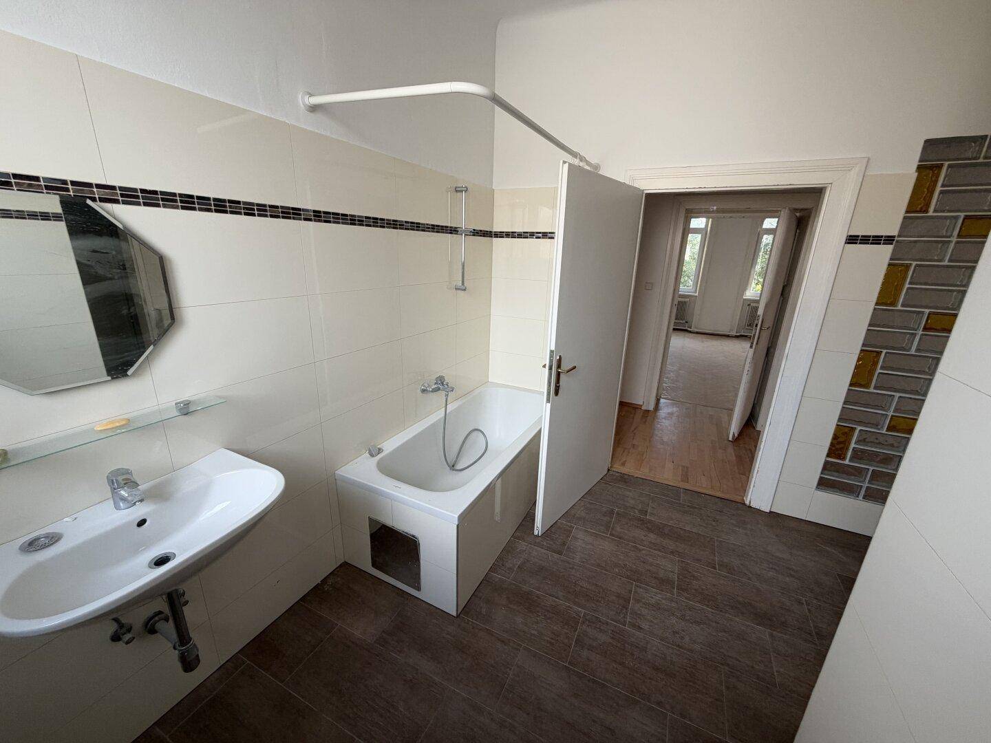 Badezimmer mit Waschbecken, Badewanne und weißen Wandfliesen, die eine Renovierung benötigen.