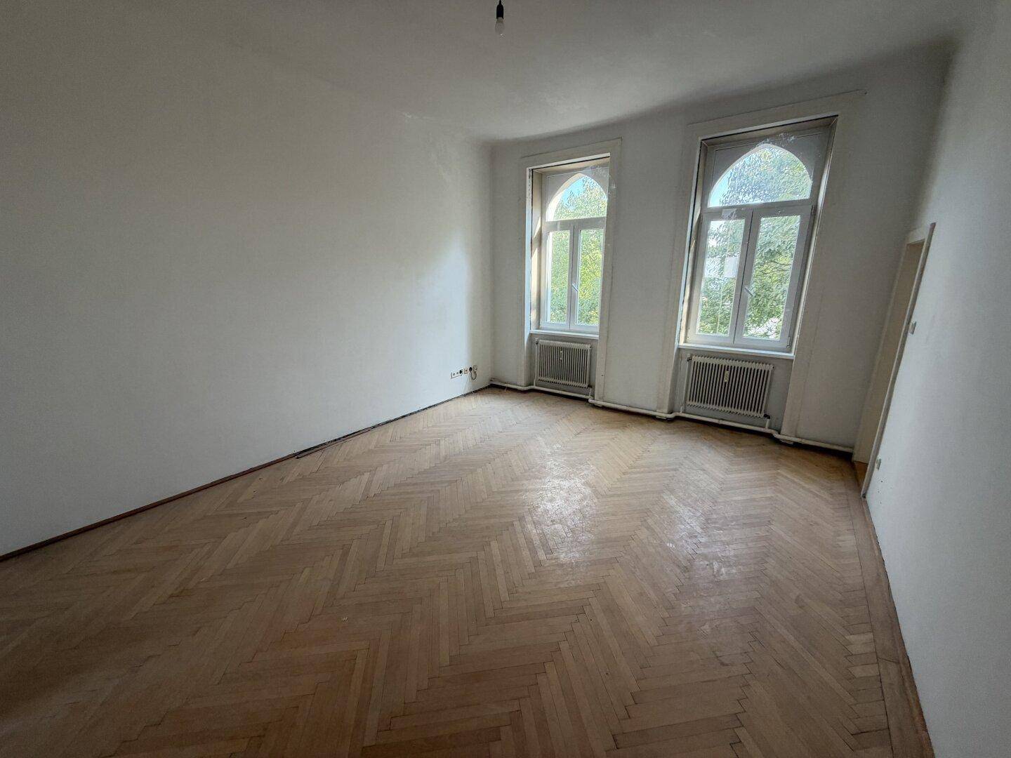 Helles Wohnzimmer mit Fischgrätparkett und hohen Bogenfenstern, die viel Licht hereinlassen.