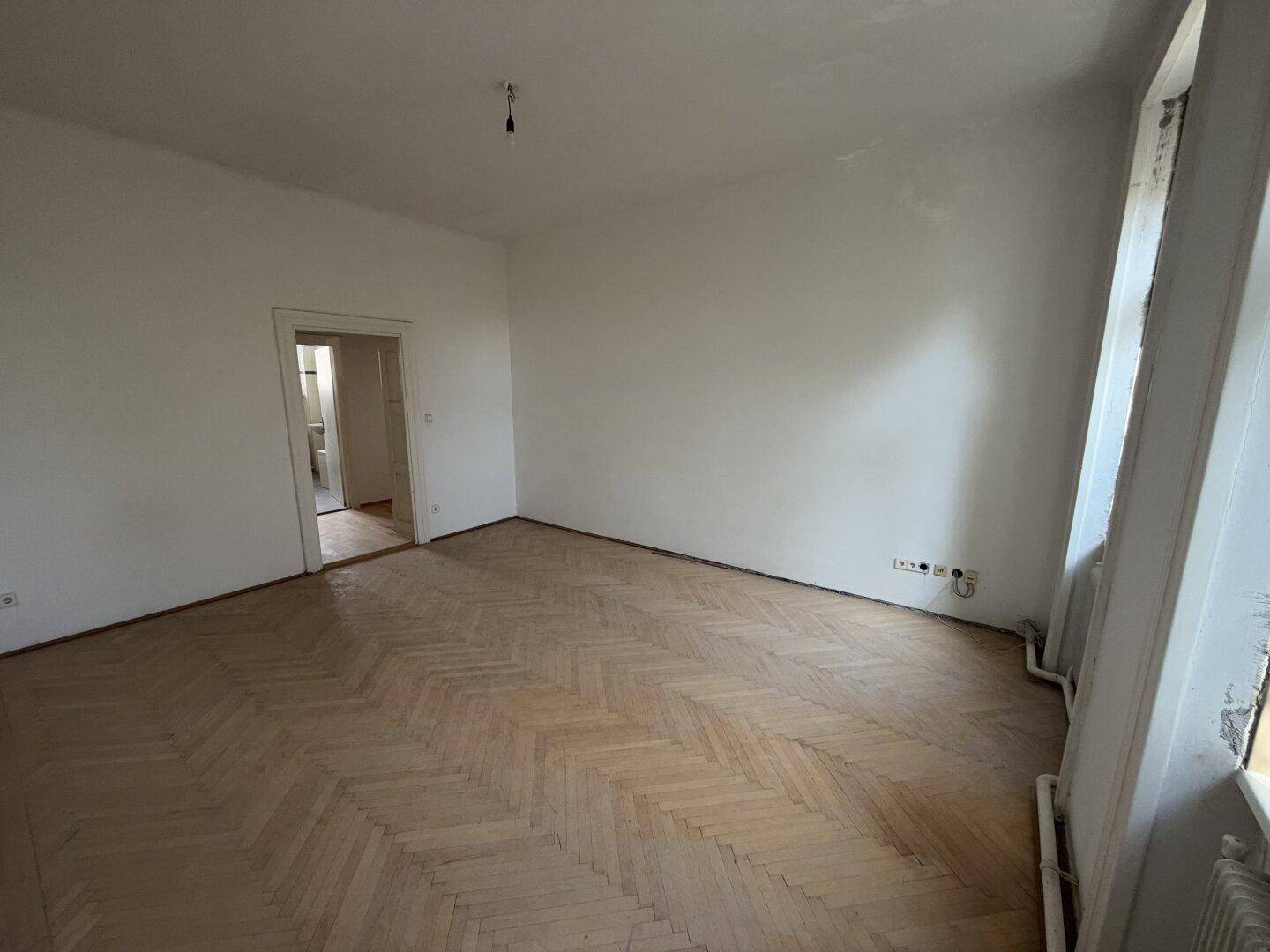 Helles Wohnzimmer mit Fischgrätparkett und Blick auf die Umgebung durch hohe Fenster.