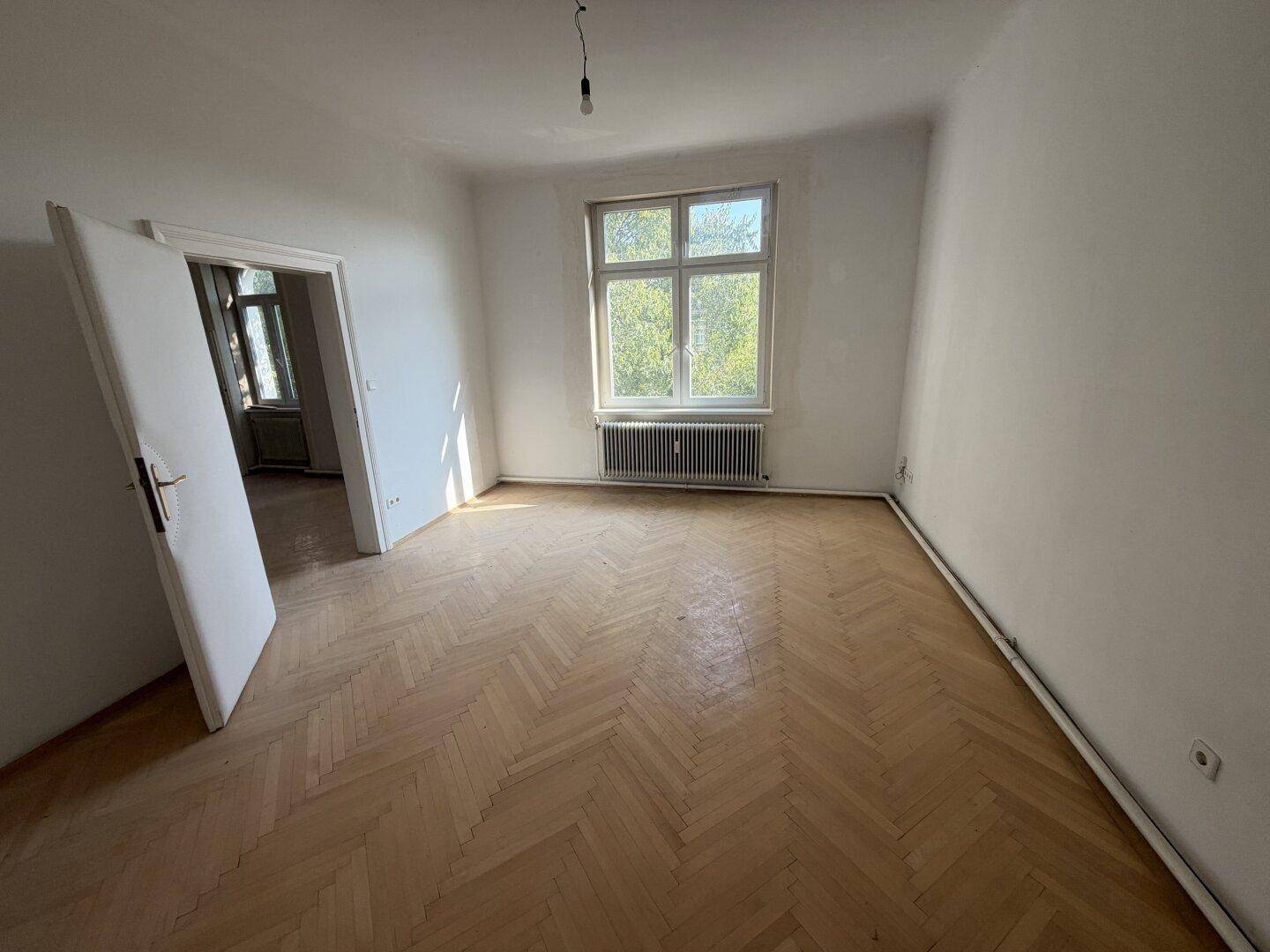 Helles Schlafzimmer mit Fischgrätparkett und einem großen Fenster, das den Raum gut belichtet.
