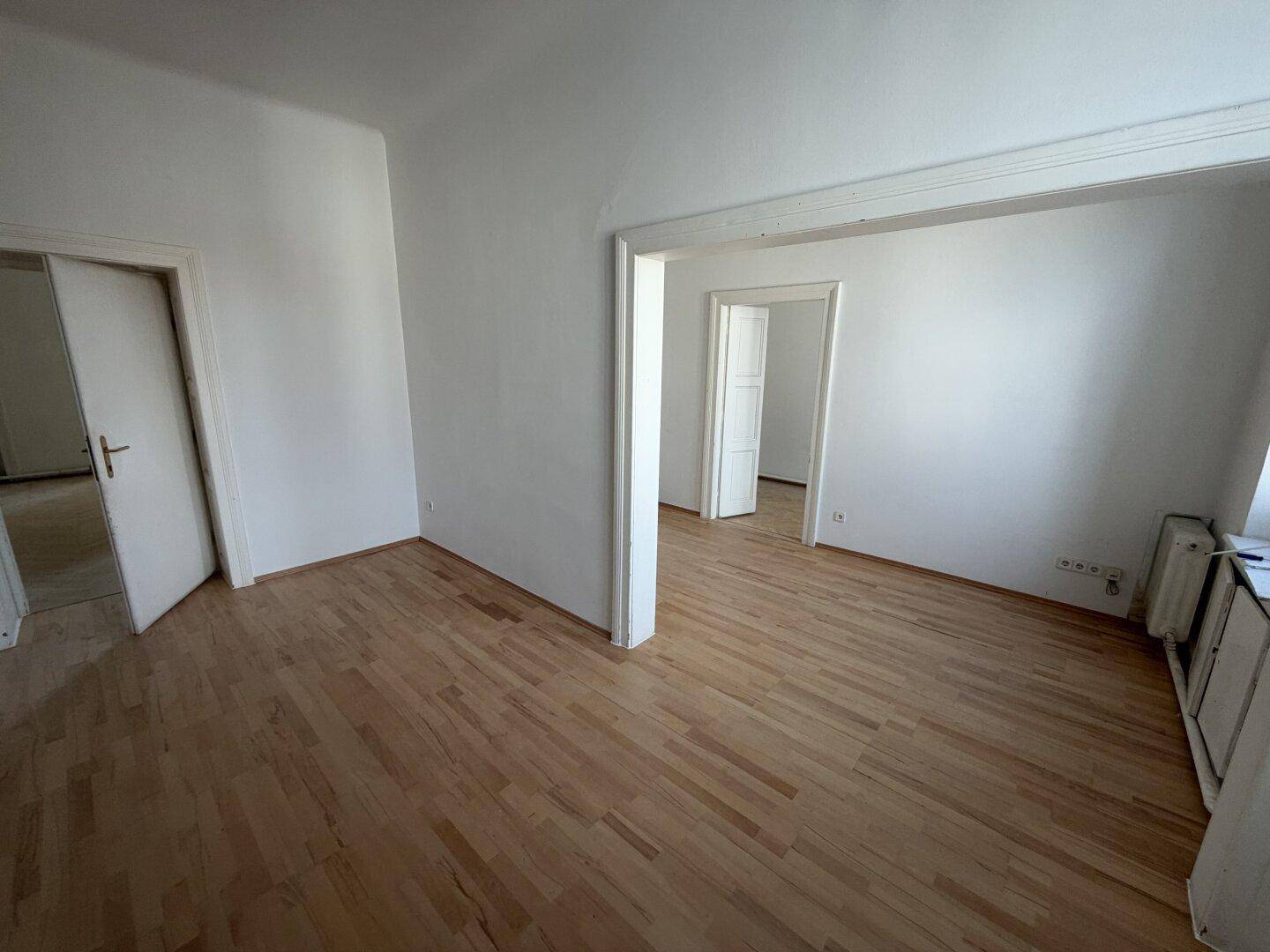 Geräumiges Wohnzimmer mit Parkettboden und mehreren Türöffnungen zu angrenzenden Räumen.