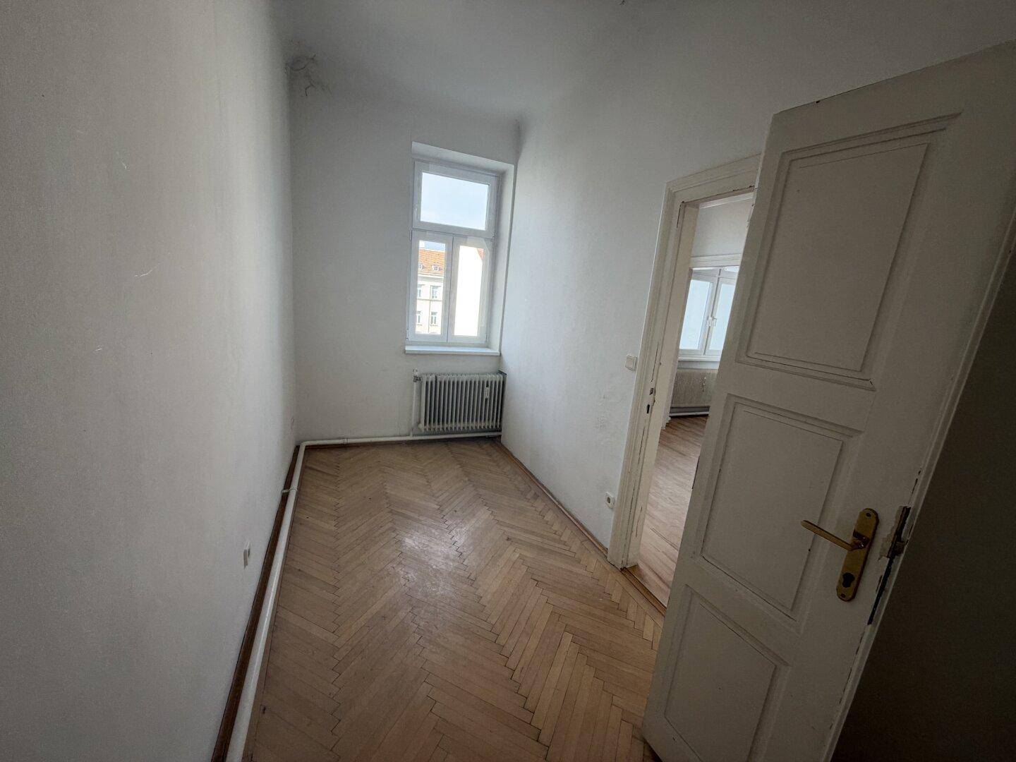 Kleines, helles Zimmer mit Fischgrätparkett und einem Fenster, ideal als Kinder- oder Arbeitszimmer.