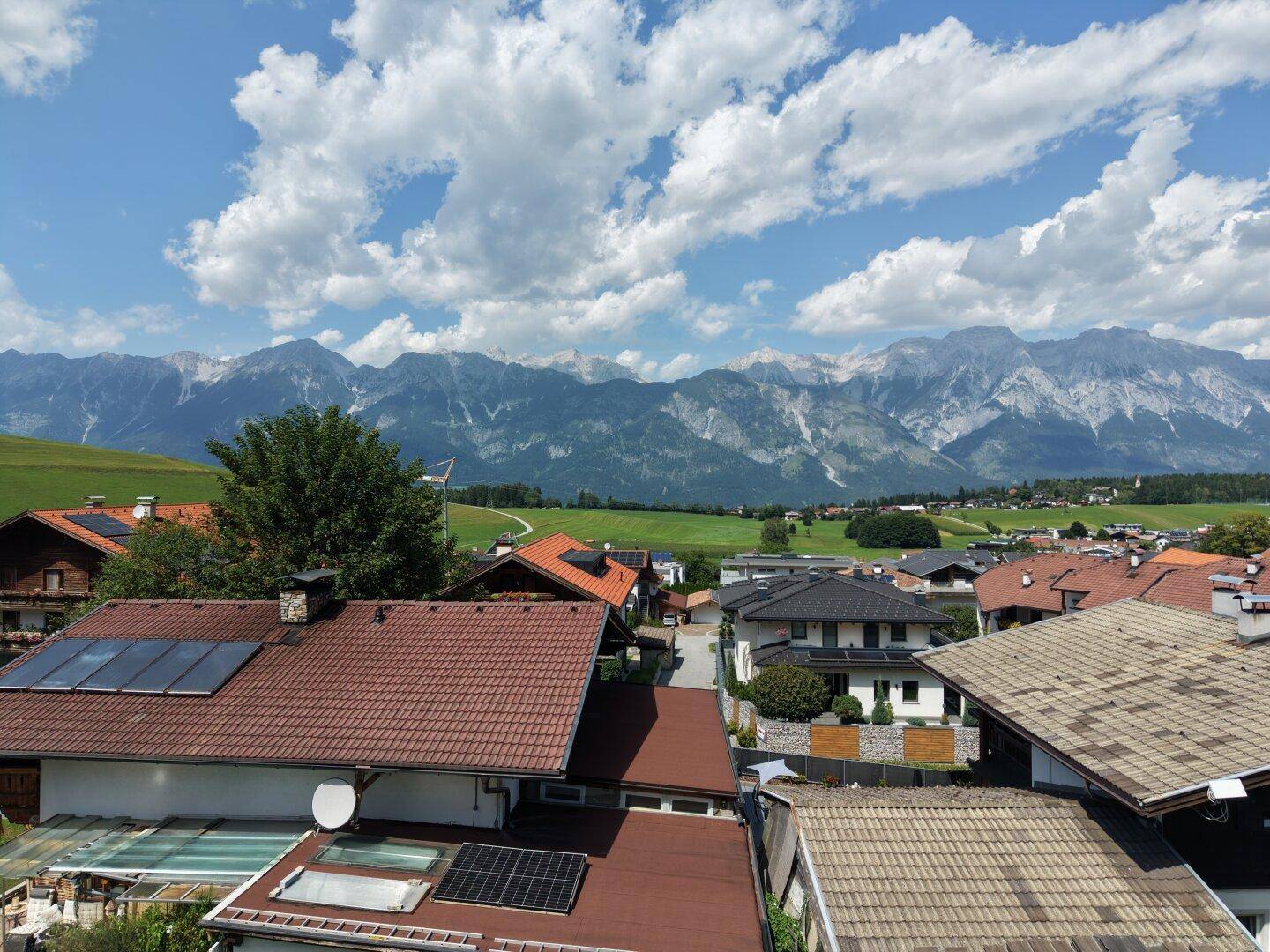 Dachlandschaft einer Wohnsiedlung mit Solaranlagen und weitem Blick auf die Alpen.