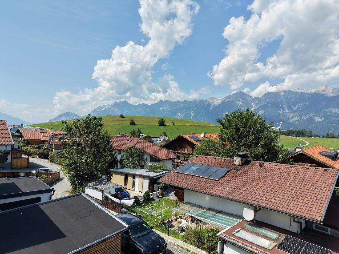 Blick über eine ländliche Wohngegend mit grünen Hügeln und ferner Bergkulisse.