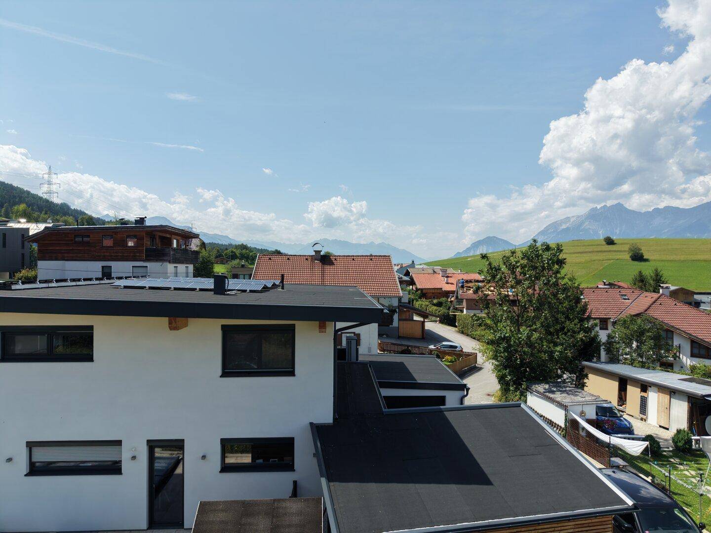 Moderne Architektur mit Flachdach und Photovoltaikanlage in einer Wohnsiedlung mit Bergblick.