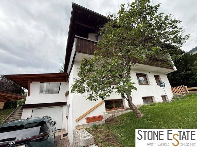 Seitenansicht des Hauses mit Garage, Balkon und einem Baum im Vordergrund.