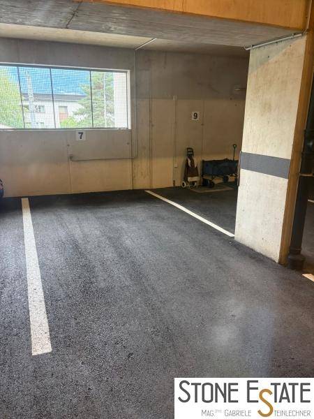 Helle Tiefgarage mit markierten Stellplätzen, Betonwänden und einem Fenster für Tageslicht.