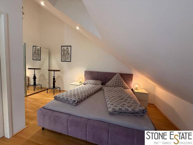 Helles Schlafzimmer mit Doppelbett, Holzboden und Spiegelschränken unter der Dachschräge.