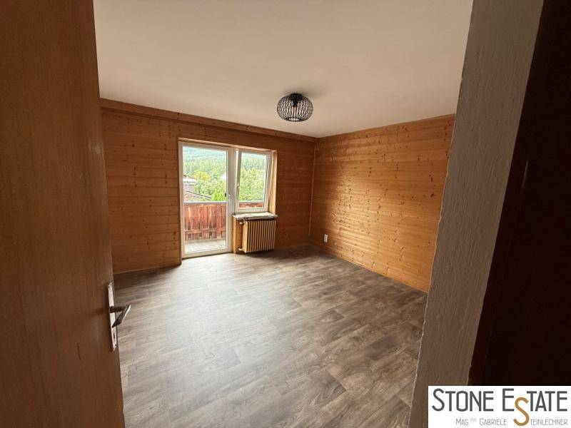 Schlafzimmer mit Holzvertäfelung, Laminatboden und Zugang zu einem Balkon.