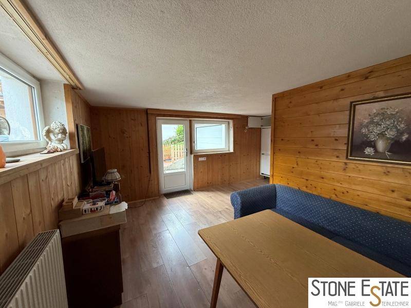 Wohnbereich mit Holzvertäfelung, Laminatboden und Zugang zu einem Außenbereich.