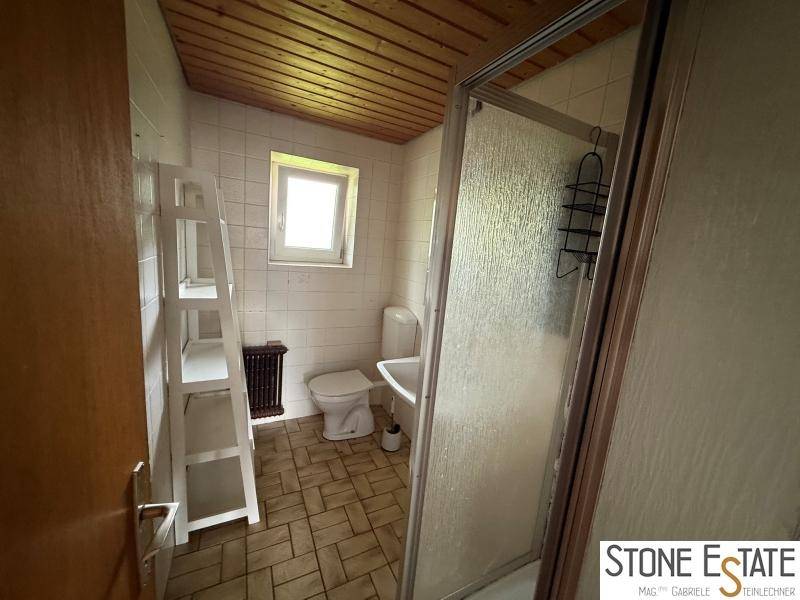 Badezimmer mit Dusche, Toilette, Waschbecken und einem Fenster für Tageslicht.