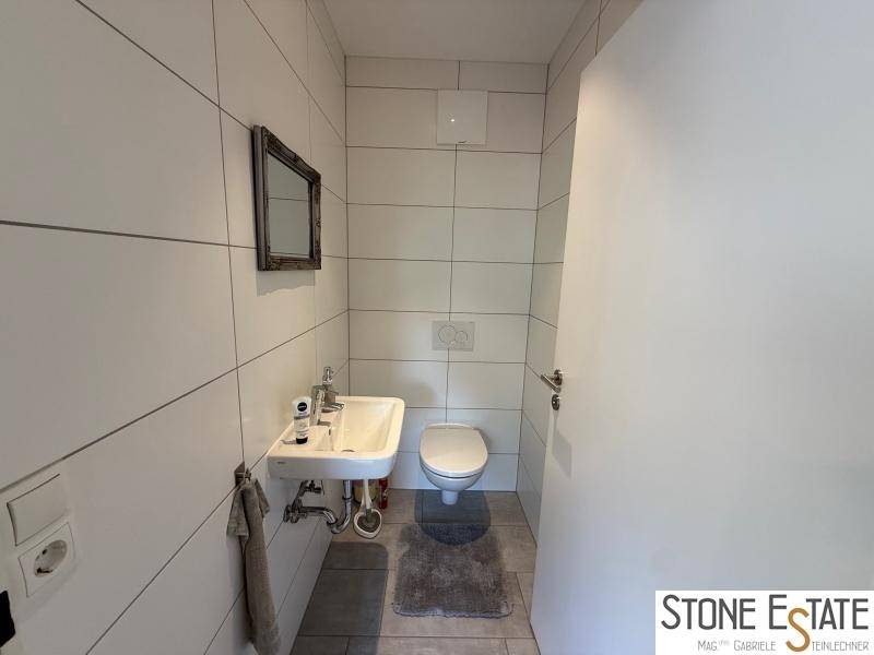 Kleines Gäste-WC mit Wand-WC, Waschbecken und weißen Fliesen.