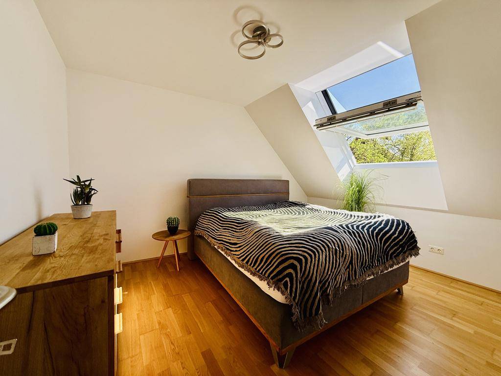 Helles Schlafzimmer mit Holzboden, Bett und großem Dachfenster unter einer Dachschräge.