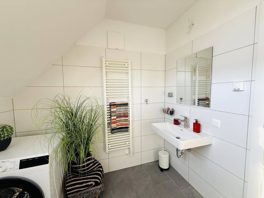 Helles Badezimmer mit modernem Waschbecken, Spiegel und weißen Fliesen.