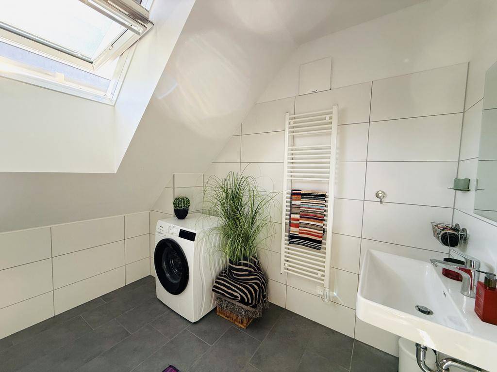 Modernes Badezimmer mit Waschmaschine, Handtuchheizkörper und Dachfenster.