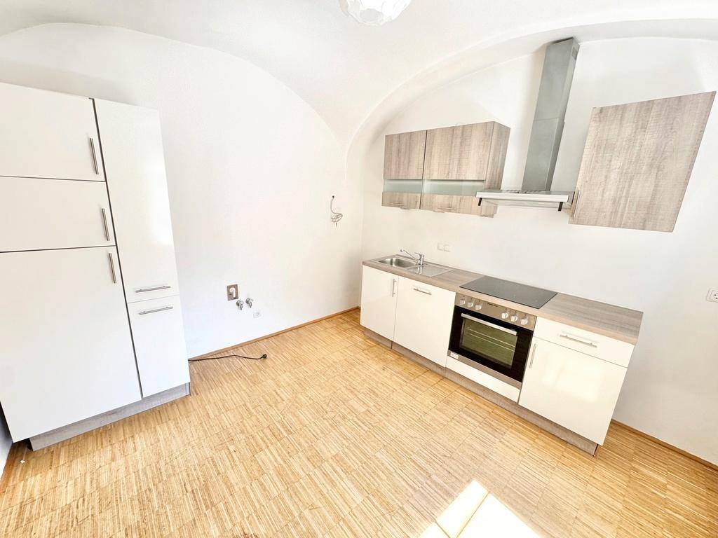 Moderne Einbauküche mit weißen und holzfarbenen Schränken, ausgestattet mit Ofen und Dunstabzugshaube.