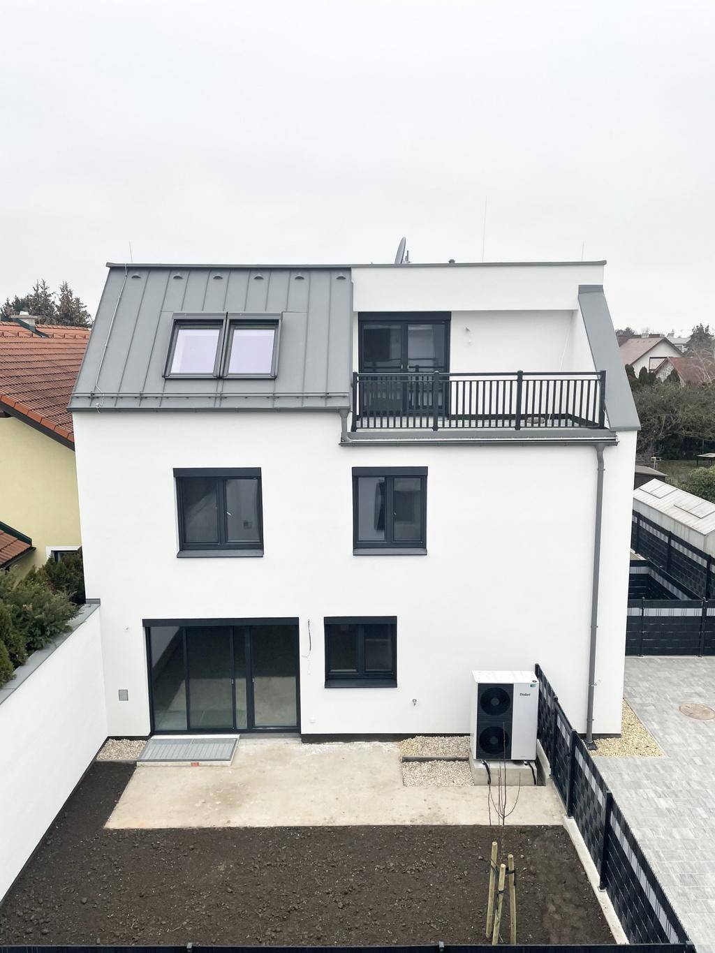 Rückansicht eines modernen Hauses mit kleiner Gartenfläche und installierter Wärmepumpe.
