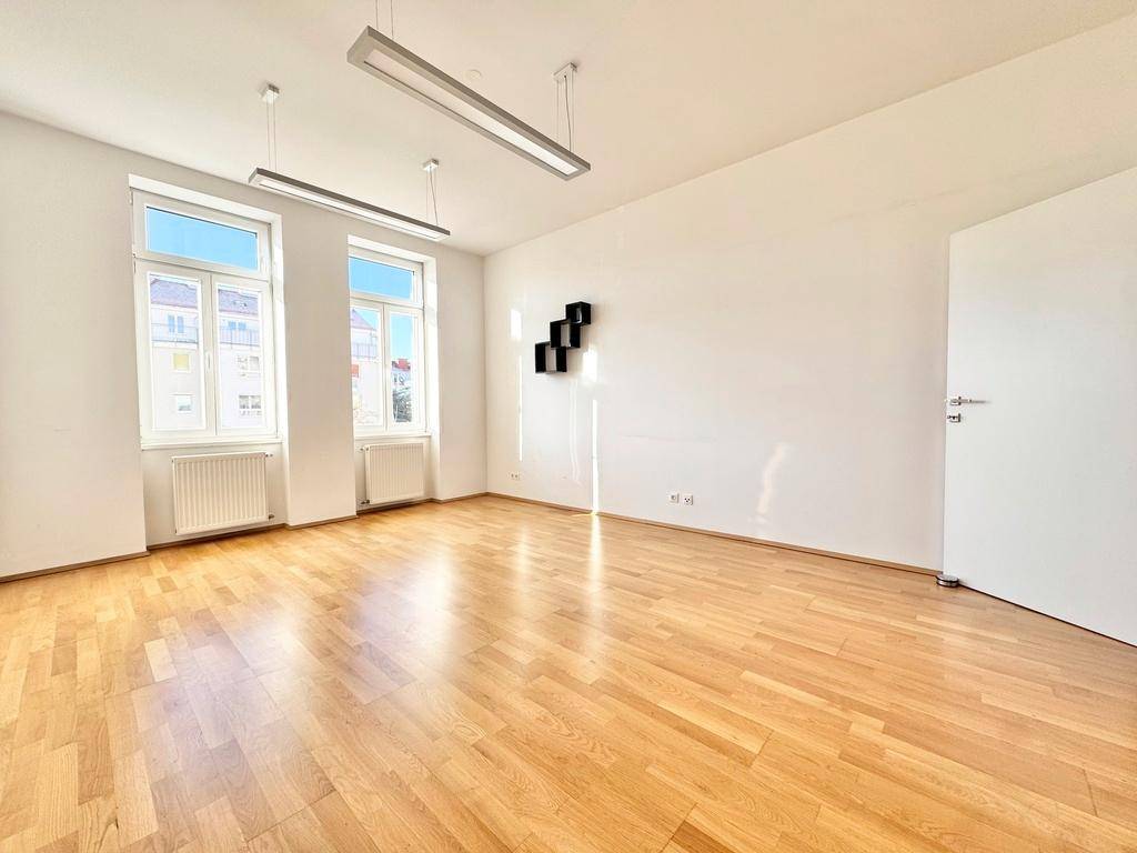 Heller Wohnraum mit Parkettboden, zwei Fenstern und einer weißen Tür, bereit zur individuellen Gestaltung.