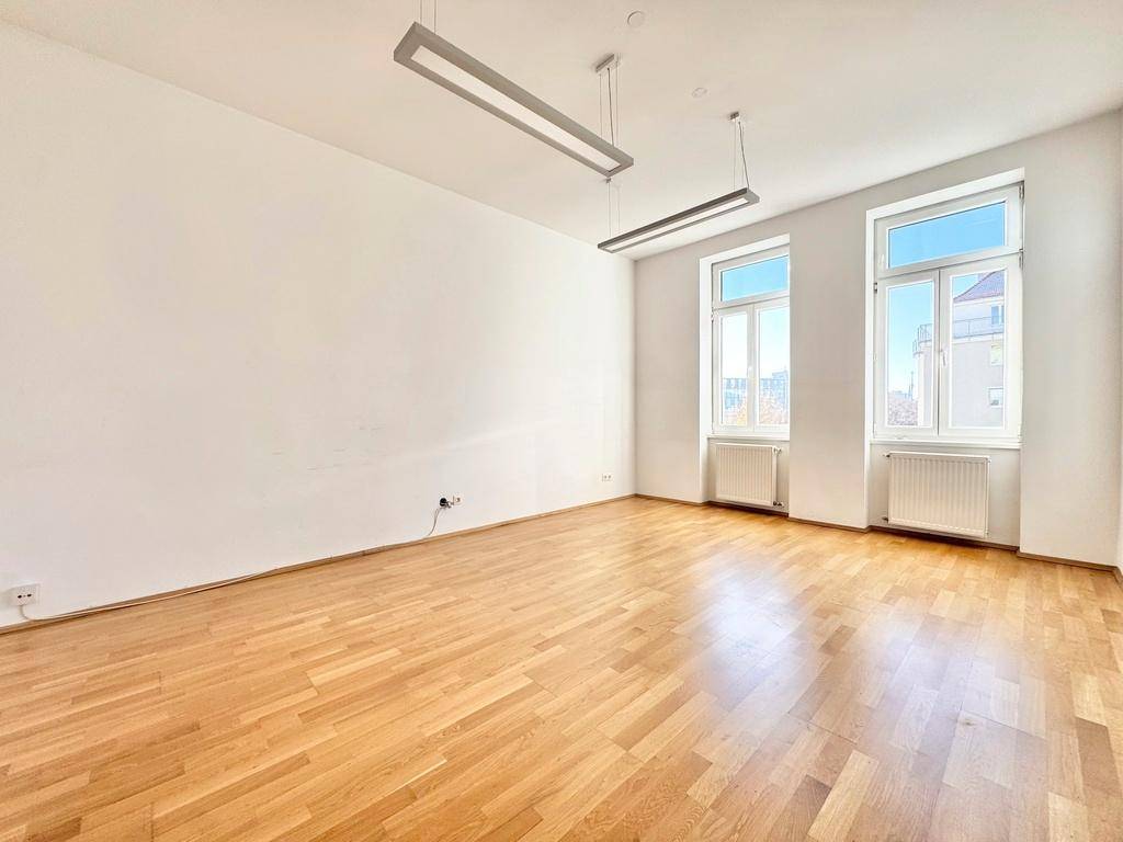Lichtdurchfluteter Raum mit glänzendem Holzboden und großen Fenstern, ideal für Wohn- oder Arbeitszwecke.