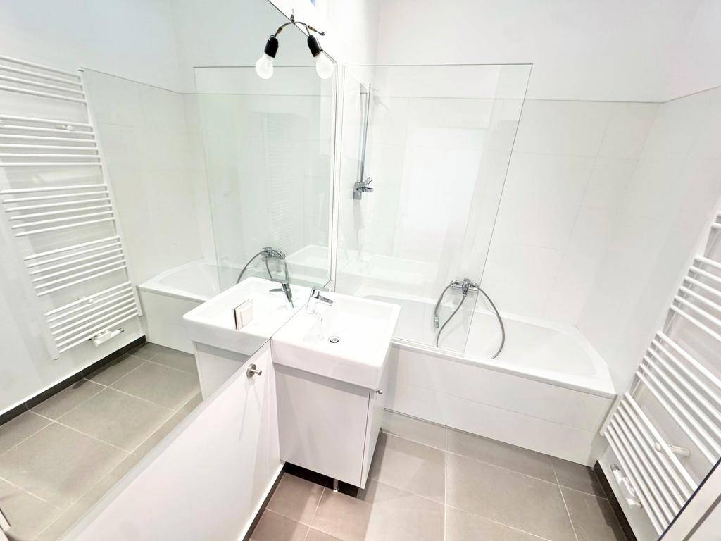 Modernes Badezimmer mit Badewanne, Einzelwaschbecken und zwei beheizten Handtuchhaltern.
