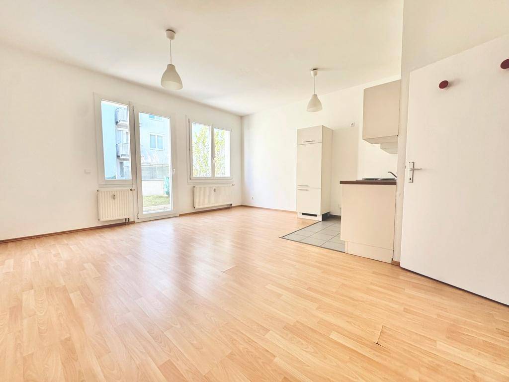 Heller, offener Wohnbereich mit Laminatboden und Zugang zum Garten, inklusive kleiner Küchenzeile.