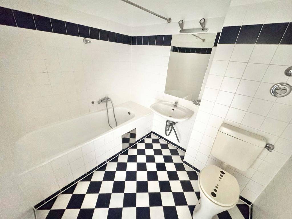 Badezimmer mit Badewanne, Waschbecken und WC, charakterisiert durch schwarz-weiß karierte Fliesen.