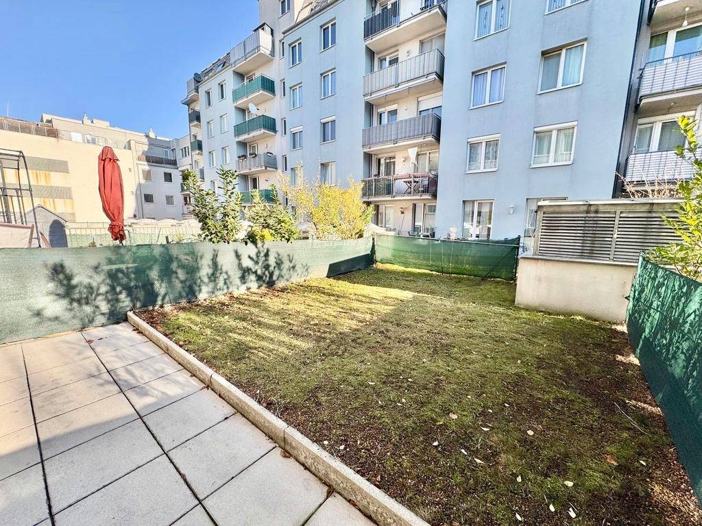 Gepflegter Gartenbereich mit Rasen und angrenzender Terrasse, umgeben von modernen Wohngebäuden.