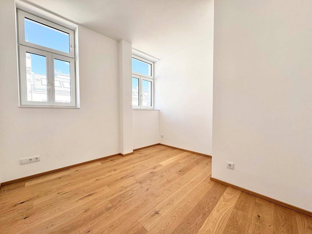 Helles Zimmer mit Holzboden und zwei Fenstern, ideal als Schlaf- oder Arbeitszimmer.