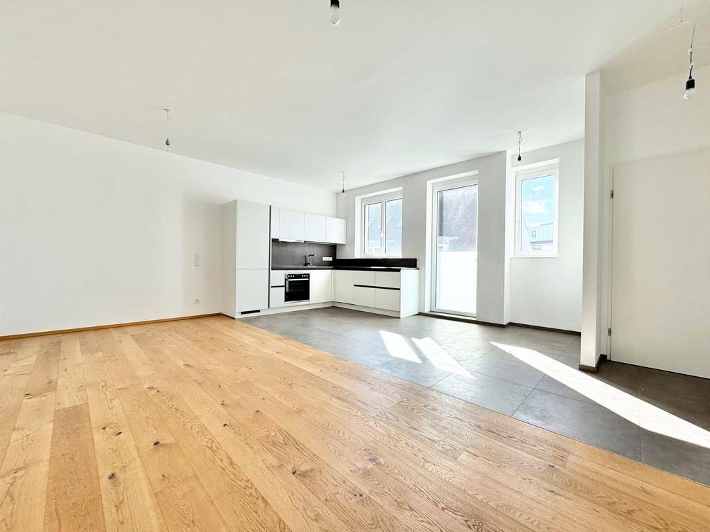 Geräumiger, offener Wohnbereich mit integrierter Küche, Holzboden und viel Tageslicht.