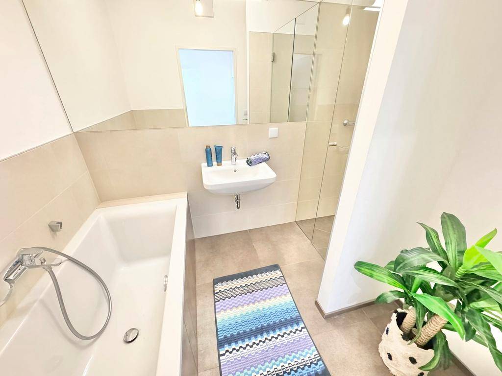 Modernes Badezimmer mit Badewanne, Dusche und großem Spiegel, hell gefliest.