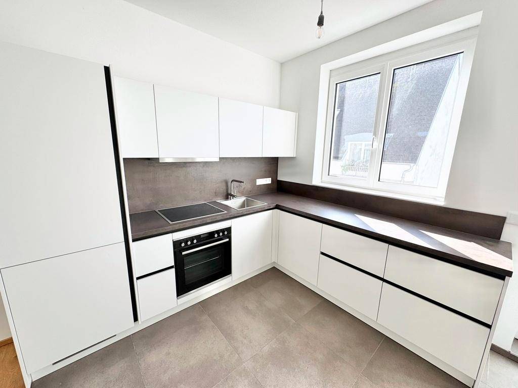 Moderne Einbauküche in Weiß mit dunkler Arbeitsplatte, Induktionskochfeld und Fenster.