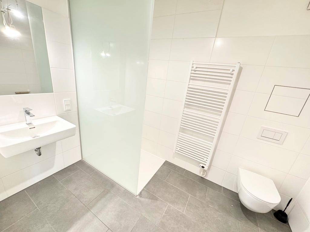 Modernes Badezimmer mit Dusche, Wand-WC, Einzelwaschbecken und praktischem Handtuchheizkörper.