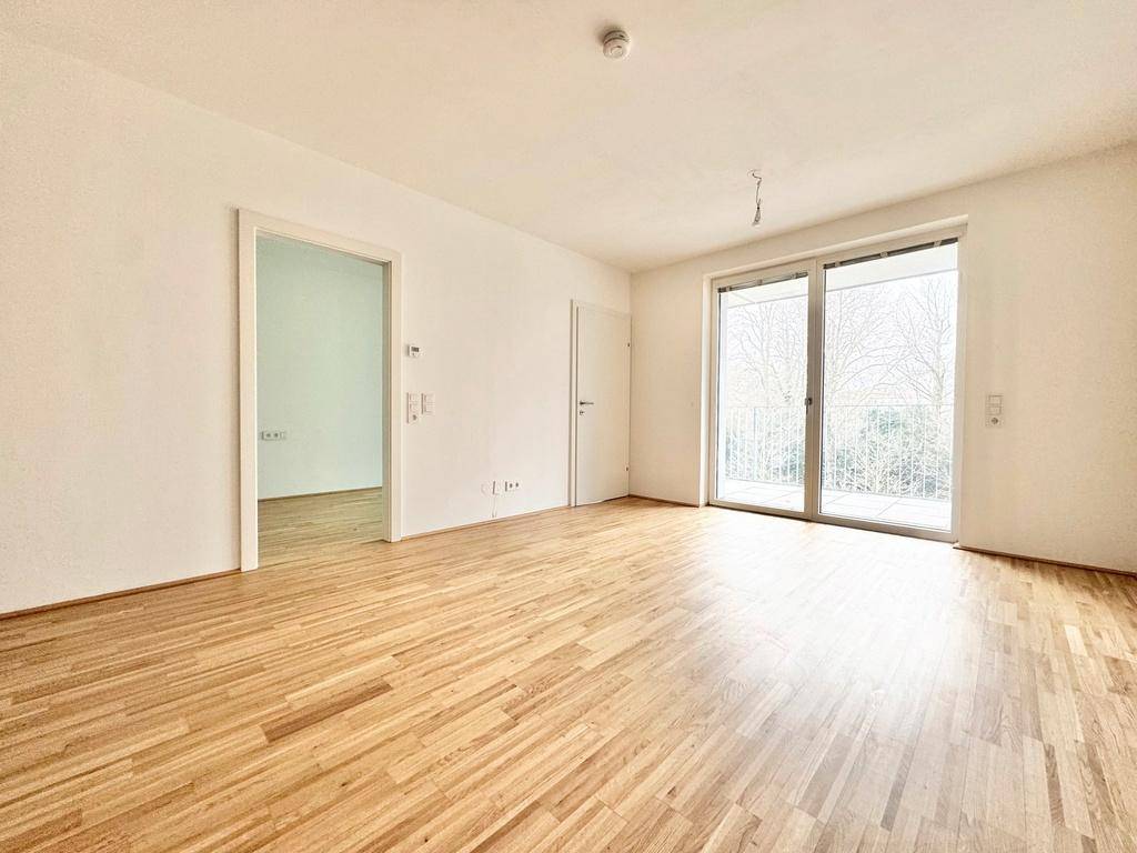 Helles Wohnzimmer mit Parkettboden und großem Fenster, das Zugang zum Balkon bietet.