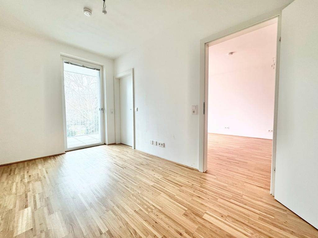 Geräumiges Zimmer mit hellem Parkettboden und großem Fenster, das viel Tageslicht hereinlässt.