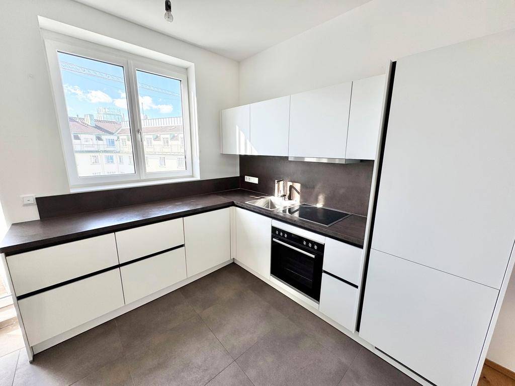 Moderne weiße Einbauküche mit dunkler Arbeitsplatte, integriertem Backofen und großem Fenster.