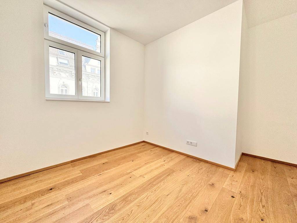 Lichtdurchflutetes Zimmer mit neuem Parkettboden und weiß gestrichenen Wänden, bereit zum Einzug.